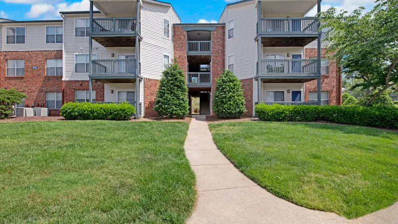A pathway leading to an apartment entrance surrounded by greenery.