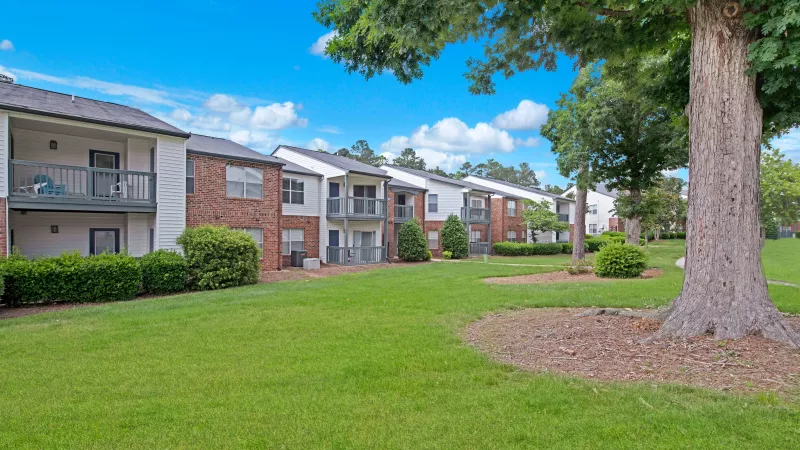 A spacious green courtyard bordered by trees and residential buildings.