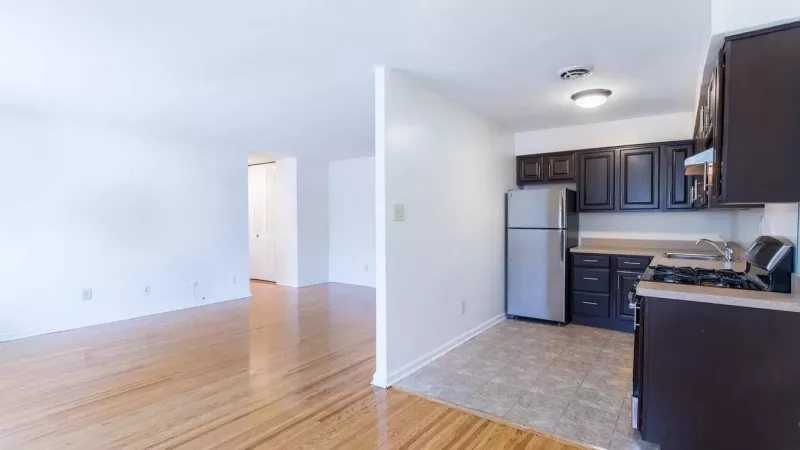 An open-concept kitchen with dark cabinetry and stainless steel appliances adjacent to a bright living area with hardwood flooring.