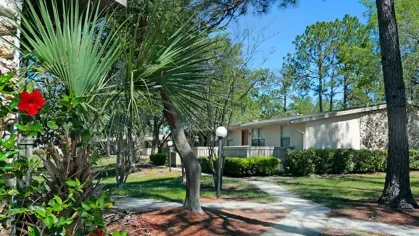 Image 2: An exterior view of an apartment building with a sidewalk and flowerbed in the foreground, surrounded by trees and greenery.