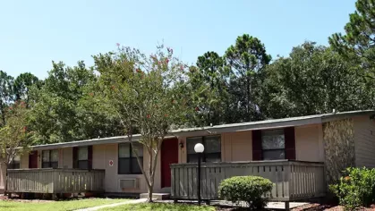 Image 6: A front view of an apartment building with a wooden deck, surrounded by trees and well-maintained landscaping, providing a welcoming atmosphere.