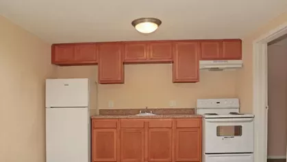 Image 7: A kitchen with a refrigerator, oven, and cabinets, featuring clean countertops and basic appliances in a small, functional space.