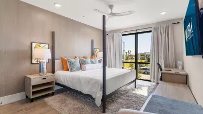 A bright and spacious bedroom with a four-poster bed, floor-to-ceiling windows, and elegant décor at Tropia Wellen Park Apartments.
