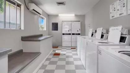 A clean and organized laundry facility at 505 West Apartments featuring multiple washers and dryers, a folding counter, and large windows for natural light.