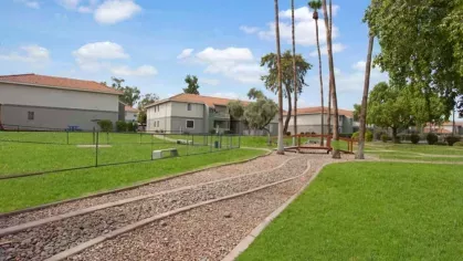 A bright and welcoming exterior featuring light-colored buildings with lush grass, trees, and palm-lined pathways at 505 West apartments.