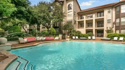Resort-style swimming pool surrounded by lush greenery and Mediterranean-style architecture.