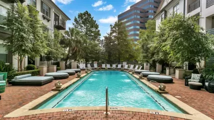 Rectangular pool with cushioned loungers, vibrant landscaping, and modern apartments in the background.