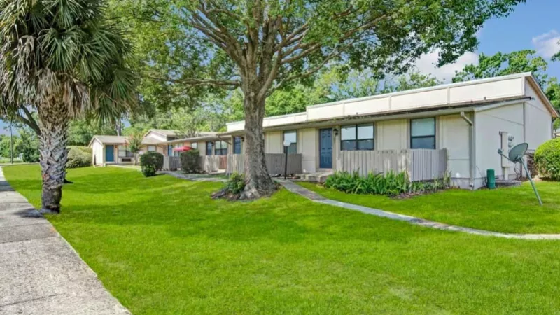 A picturesque view of single-story apartment homes with private patios, surrounded by greenery and bright open spaces.