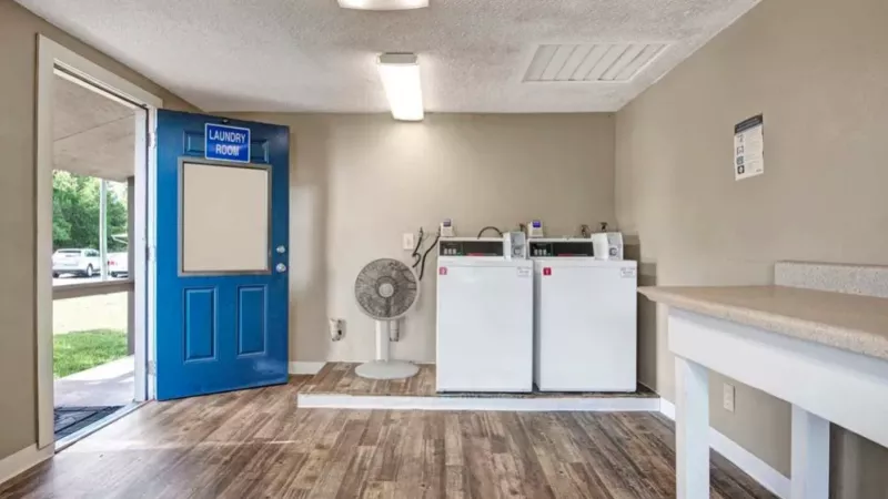 A spacious laundry room with a blue entrance door labeled "Laundry Room," showcasing two white dryers and folding areas.