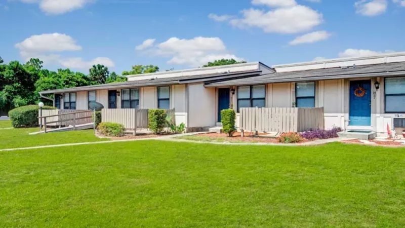 A peaceful apartment community with a central green area, individual entrances, and bright blue doors.