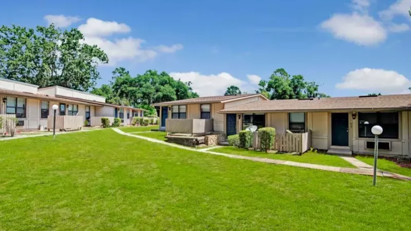 A peaceful apartment community with a central green area, individual entrances, and bright blue doors.