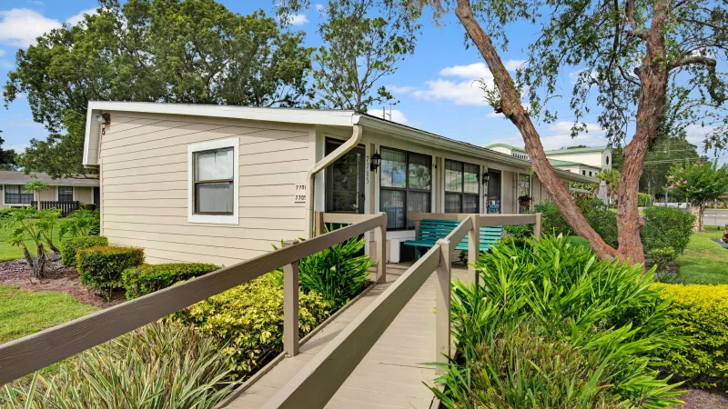 A ramp with wooden railings leads to a charming apartment entry surrounded by landscaped greenery.