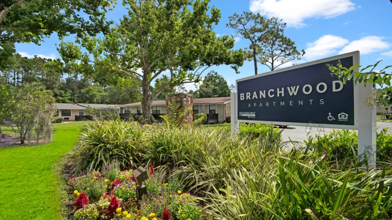A landscaped entrance sign for Branchwood Apartments surrounded by colorful flowers and trees.