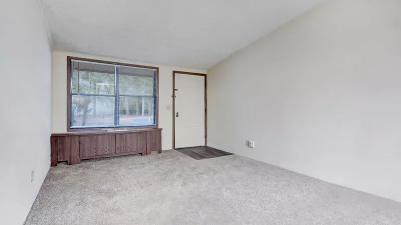 Bright and carpeted living area at Bridgepoint Apartments with built-in shelving and large window for natural light.