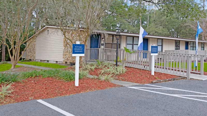 Front entrance of Bridgepoint Apartments with a vibrant blue door and trimmed greenery.