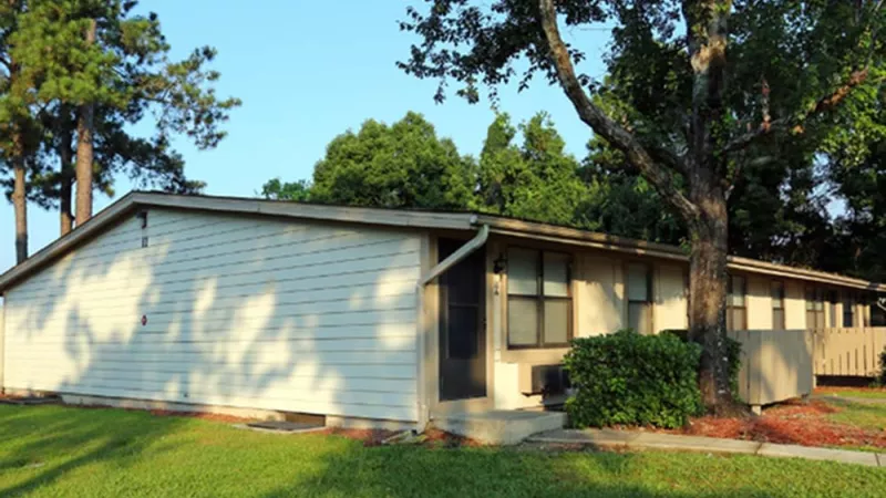 A quiet single-story apartment building with light-colored siding, surrounded by lush green lawns and mature trees. This image highlights the peaceful and natural environment at Broadview Oaks Apartments.