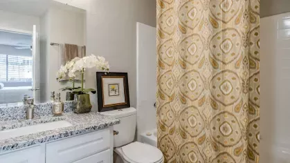 A clean and elegant bathroom featuring granite counters, a large mirror, and decorative details.