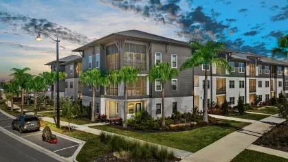Exterior view of the apartments at dusk, highlighting modern architecture, lush landscaping, and well-lit pathways.