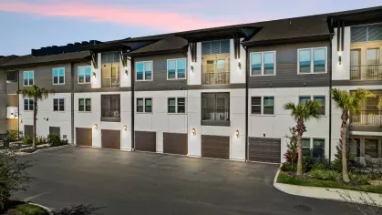 Exterior view of the apartments at dusk, highlighting modern architecture, lush landscaping, and well-lit pathways.