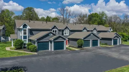 Aerial view of a stylish apartment community featuring multiple townhome-style buildings with attached garages. The surrounding greenery and open parking spaces create a welcoming and serene environment.