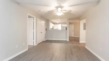 A spacious open-concept living area with wood-style flooring and ceiling fan, leading to a modern kitchen with white cabinets and stainless steel appliances.