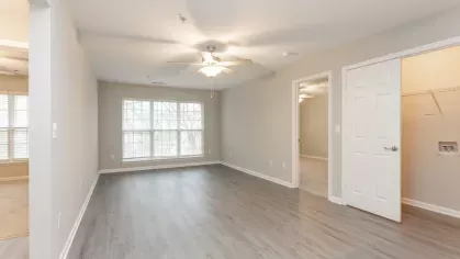 A spacious open-concept living area with wood-style flooring and ceiling fan, leading to a modern kitchen with white cabinets and stainless steel appliances.