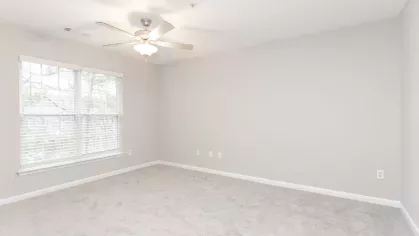 A cozy carpeted bedroom with a ceiling fan, a large window for natural light, and a spacious closet for added storage.