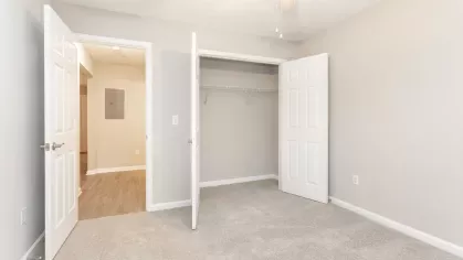 A cozy carpeted bedroom with a ceiling fan, a large window for natural light, and a spacious closet for added storage.
