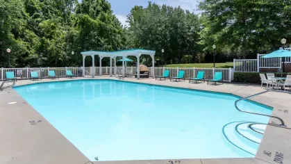 A sparkling outdoor swimming pool surrounded by lounge chairs and shaded cabanas, set amidst mature trees for a relaxing atmosphere.