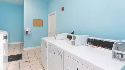 Interior view of a modern laundry facility at Heritage Apartments, featuring bright blue walls and commercial-grade washing and drying machines.