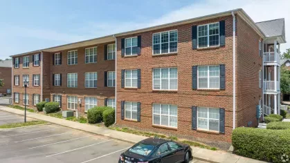 A close-up of a red brick apartment building at Heritage Apartments, highlighting its black shutters, white trim, and spacious windows.