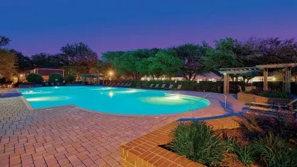 Evening view of the illuminated pool area at Maple Bay Apartments, surrounded by trees and ambient lighting for a serene ambiance.