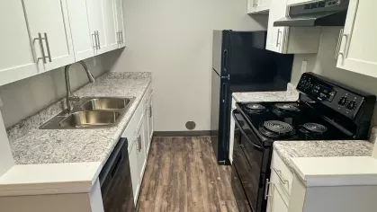  Updated galley kitchen with white shaker cabinets, black appliances, granite-style countertops, and wood-style flooring.