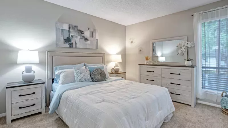 Elegant bedroom at Norcross Crossings Apartments with cozy bedding, soft lighting, and large windows for natural light and comfort.