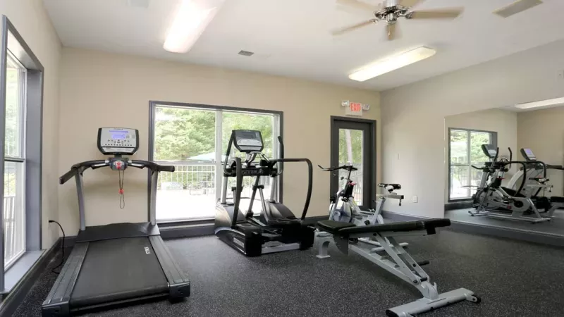 A fully equipped fitness center at Norcross Crossings Apartments featuring modern exercise machines, free weights, and yoga balls, with large windows providing natural light.