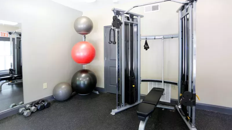 A fully equipped fitness center at Norcross Crossings Apartments featuring modern exercise machines, free weights, and yoga balls, with large windows providing natural light.
