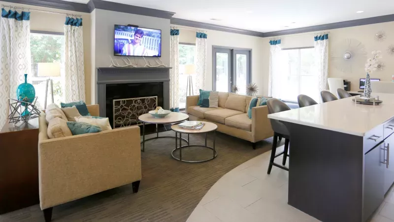 A stylish clubhouse at Norcross Crossings Apartments with cozy seating, a fireplace, and a kitchen area, perfect for social gatherings and relaxation.