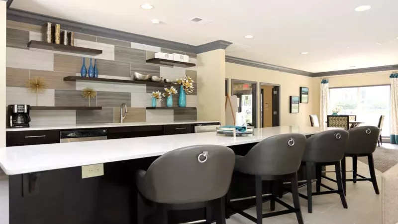 A stylish clubhouse at Norcross Crossings Apartments with cozy seating, a fireplace, and a kitchen area, perfect for social gatherings and relaxation.