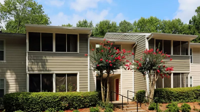 A serene apartment building at Norcross Crossings Apartments, surrounded by lush green landscaping and tall trees, offering a peaceful living environment.