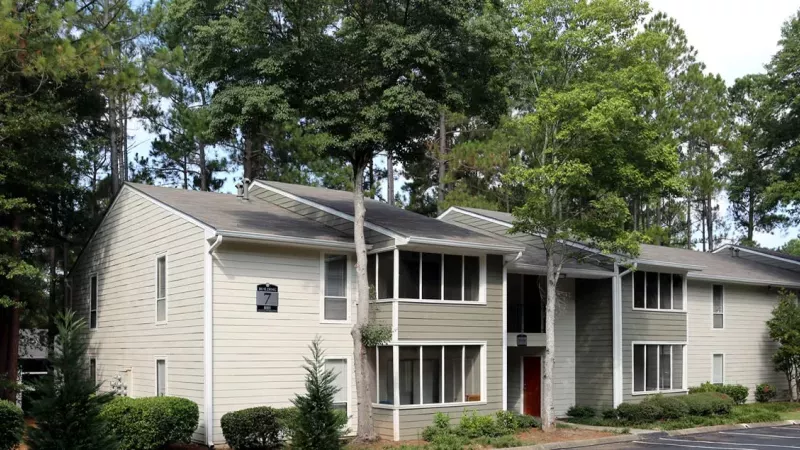 A charming exterior view of Norcross Crossings Apartments, with vibrant landscaping and tall, shady trees.