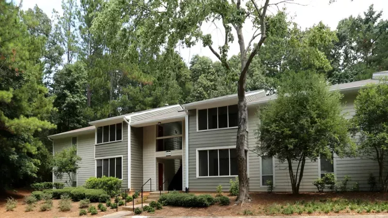 A charming exterior view of Norcross Crossings Apartments, with vibrant landscaping and tall, shady trees.