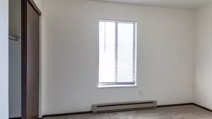 A cozy bedroom featuring a built-in closet with wooden sliding doors, soft carpet flooring, and minimalist décor, offering a peaceful retreat at North River Place Apartments.