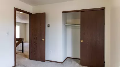 A cozy bedroom featuring a built-in closet with wooden sliding doors, soft carpet flooring, and minimalist décor, offering a peaceful retreat at North River Place Apartments.