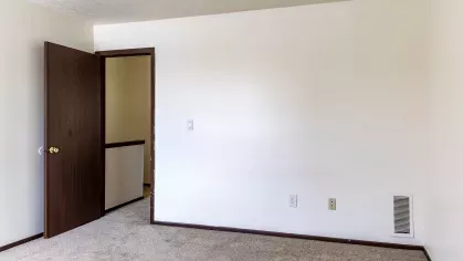 A bright and spacious bedroom with natural light pouring through a large window, complemented by clean beige walls and plush carpeting, ideal for comfort and relaxation.