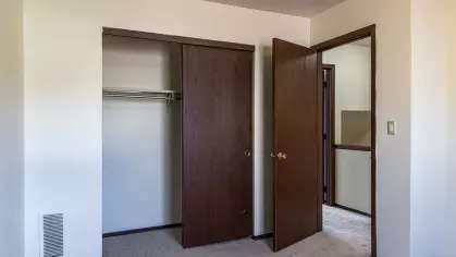 A cozy bedroom featuring a built-in closet with wooden sliding doors, soft carpet flooring, and minimalist décor, offering a peaceful retreat at North River Place Apartments.