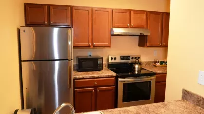 A modern kitchen at North River Place Apartments featuring stainless steel appliances, wooden cabinetry, and a polished countertop