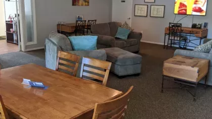 A cozy clubhouse with comfortable sofas, a dining area, and a mounted TV, creating an inviting space for residents to gather and relax