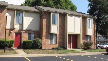 A clean and spacious view of North River Place Apartments' brick townhomes, accented with bright red doors and manicured landscaping