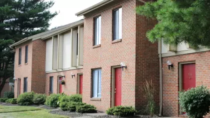 A red brick apartment building with neatly trimmed hedges, vibrant flowers, and reserved parking spaces at North River Place Apartments