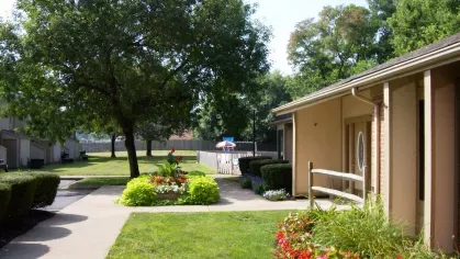 The rental office at North River Place Apartments, surrounded by colorful flower beds and shaded by mature trees